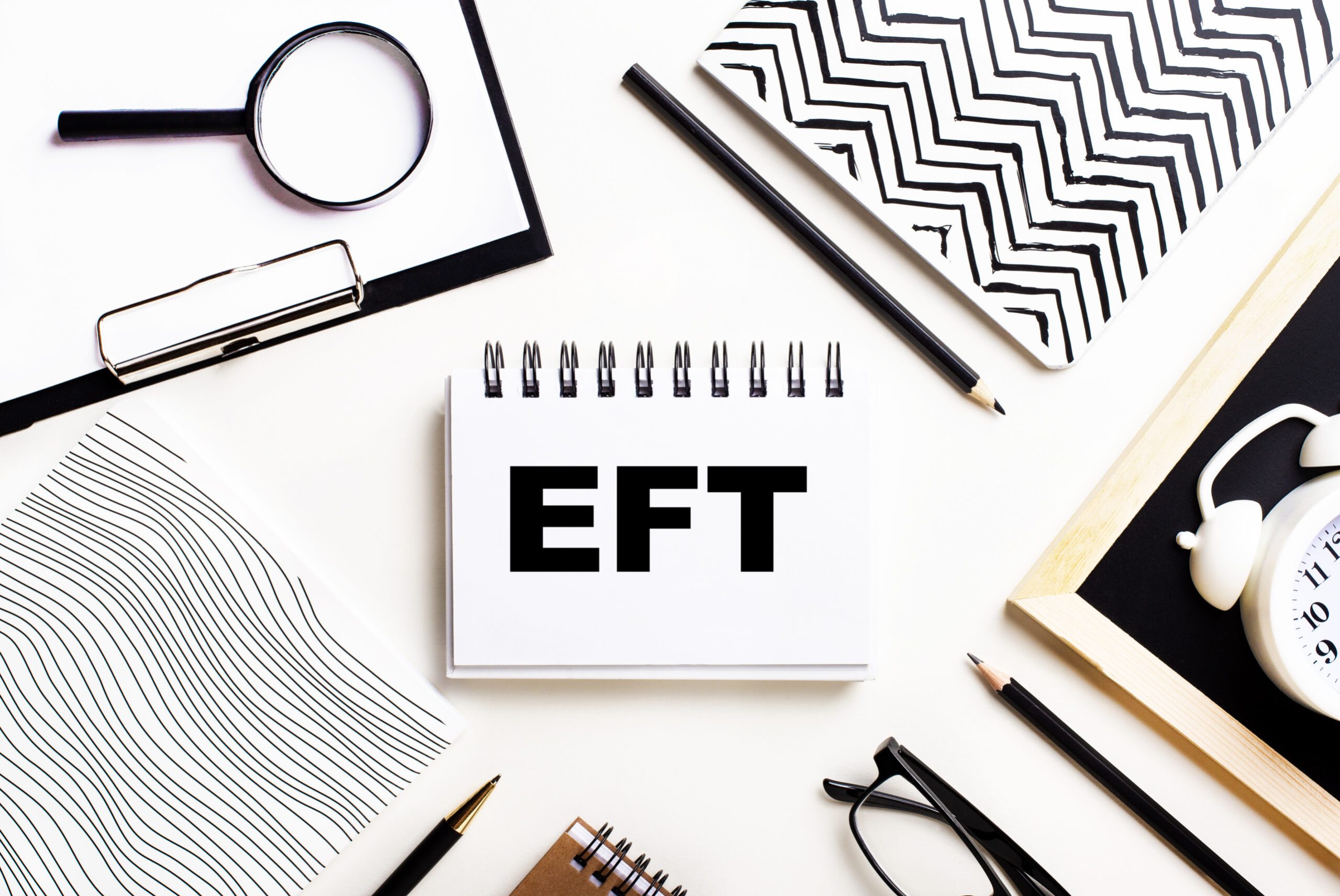 On a light table are notebooks, a magnifying glass, an alarm clock, glasses, and a pen. And in the center is a notebook with the text EFT